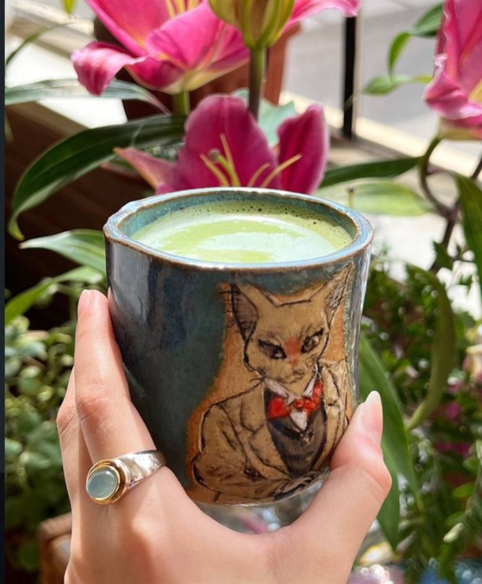 Deep blue glazed tumbler filled with matcha, carved with an elegant cat wearing a suit and red bow tie.